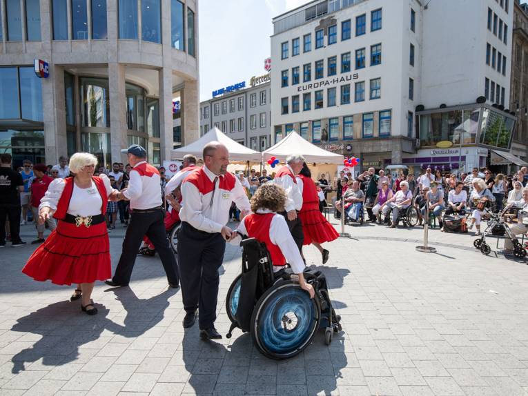 Vier Paare - teilweise mit Rollstuhl - in Tanzkostümen bei einer Square Dance-Vorführung auf dem Kröpcke
